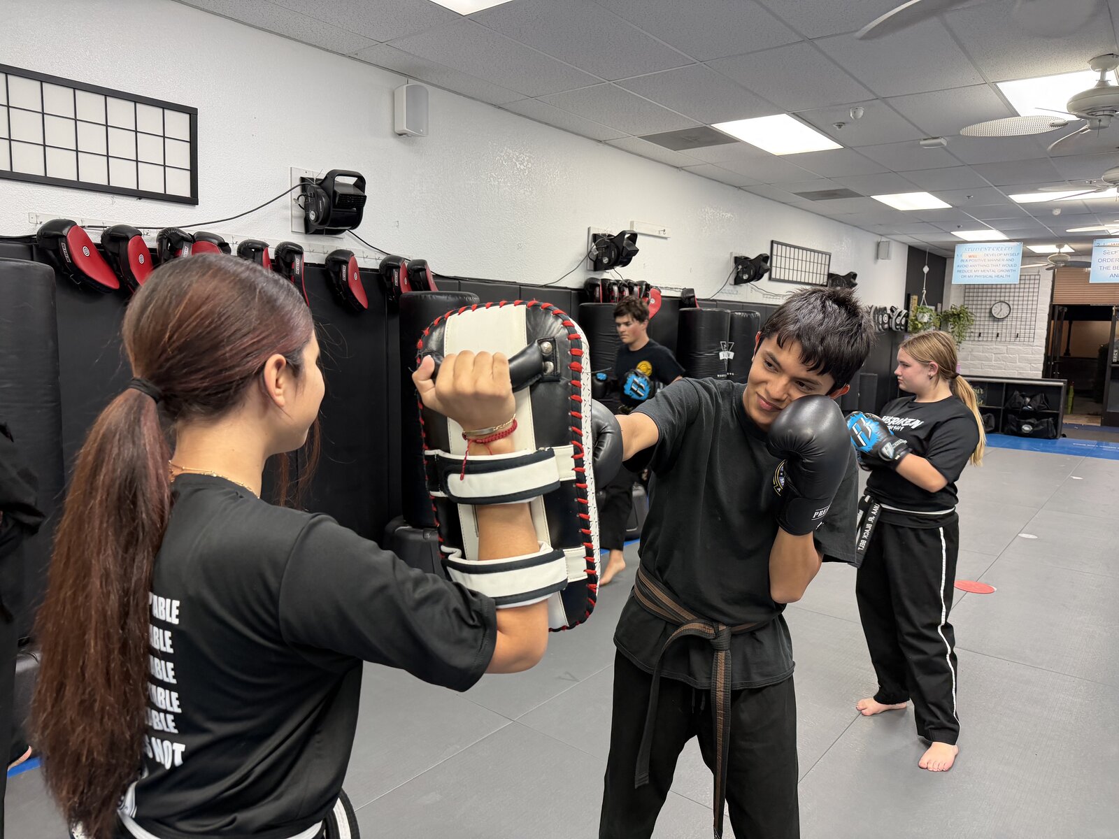 A Junior Warriors student in boxing gloves punching a striking pad held by a training partner